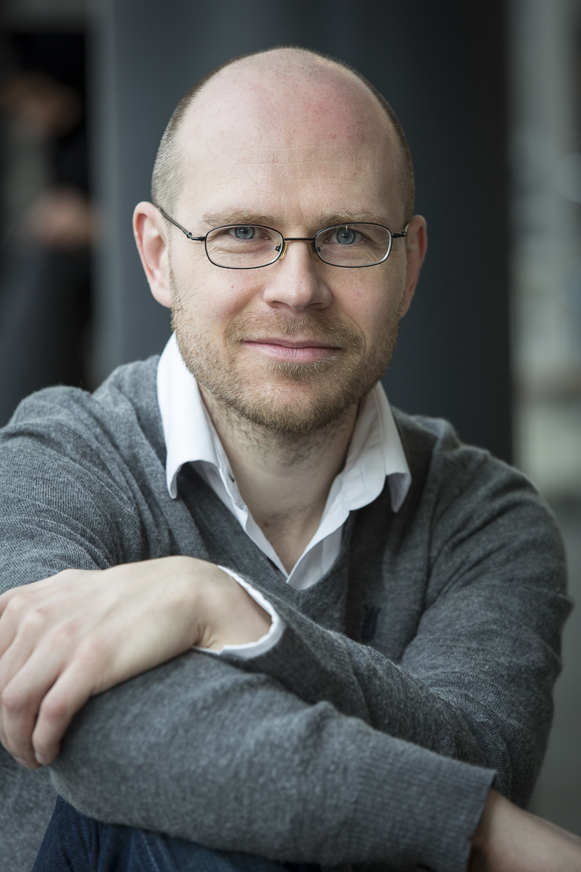 porträtt av Jesper i grå tröja med ljus skjorta. Jesper är snabbad, har glasögon och mycket kort skägg. an 